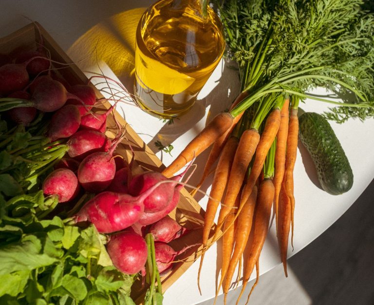 A vibrant display of fresh vegetables and oil on a white table, with shadows cast in the sunlight.