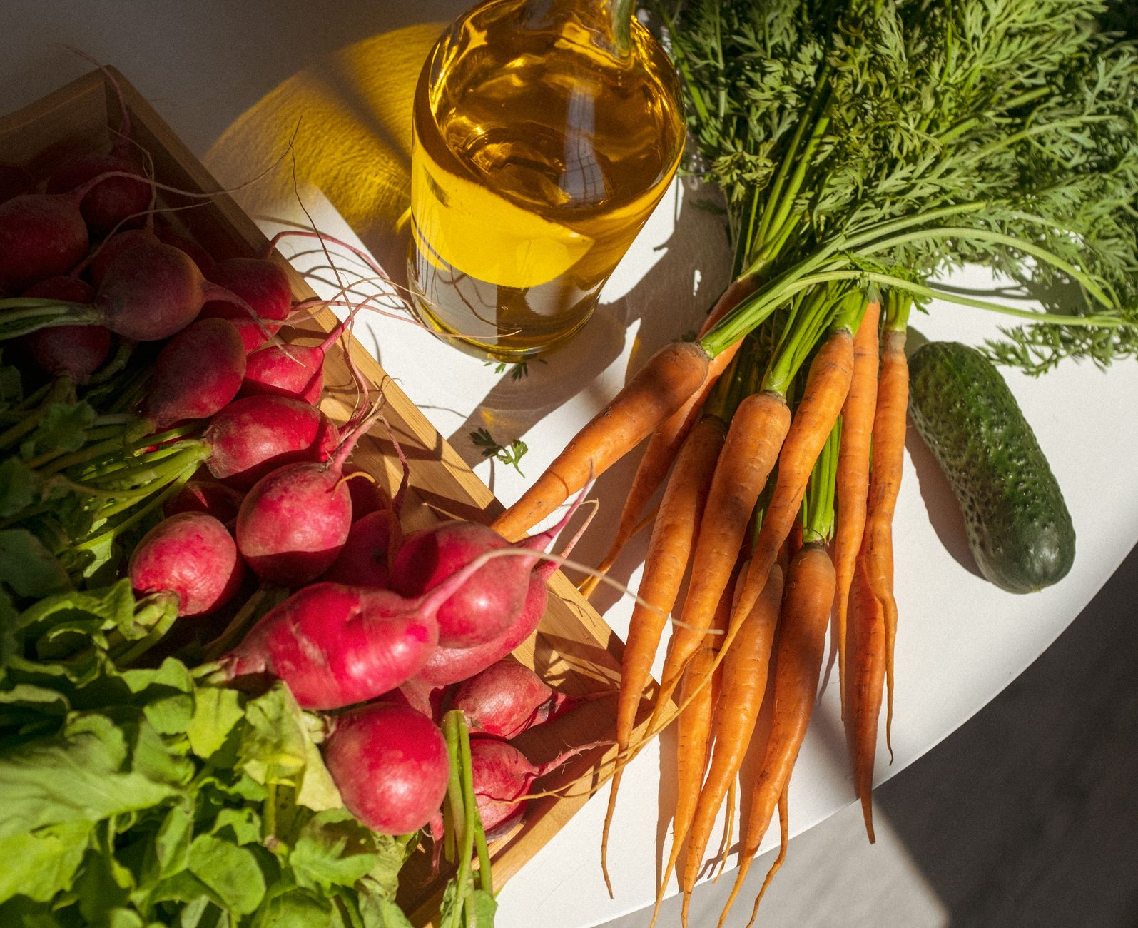 A vibrant display of fresh vegetables and oil on a white table, with shadows cast in the sunlight.