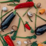 A colorful assortment of fresh vegetables including eggplants, peppers, and mushrooms on a flat surface.