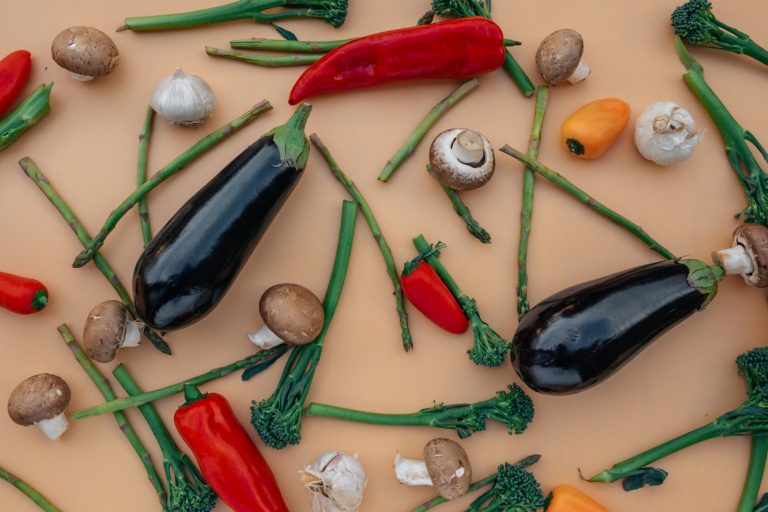 A colorful assortment of fresh vegetables including eggplants, peppers, and mushrooms on a flat surface.